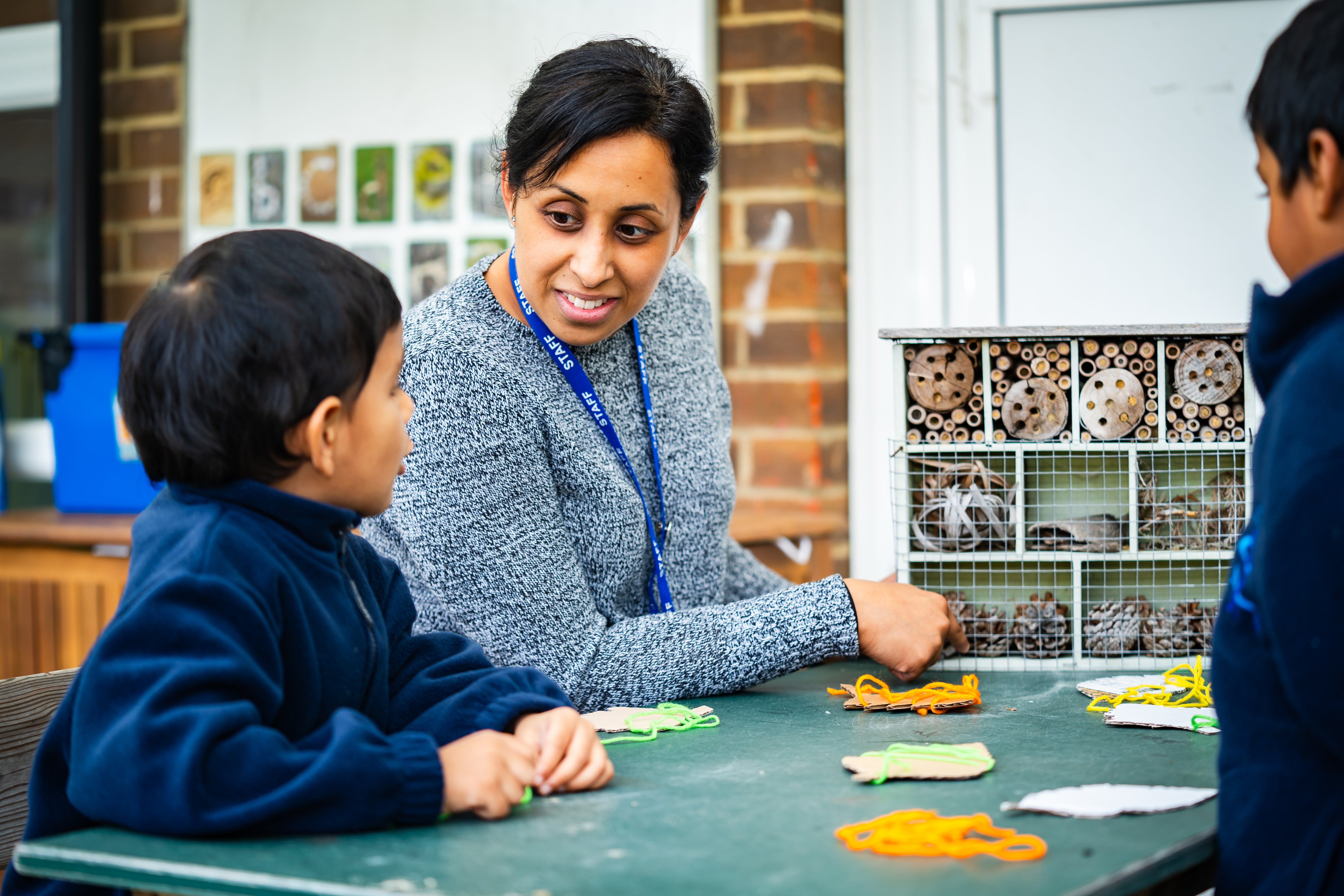 A female teacher engaging with two young pupils at St Martin's at a table within a classroom.
